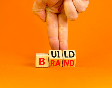 A hand arranges blocks spelling BUILD BRAND.